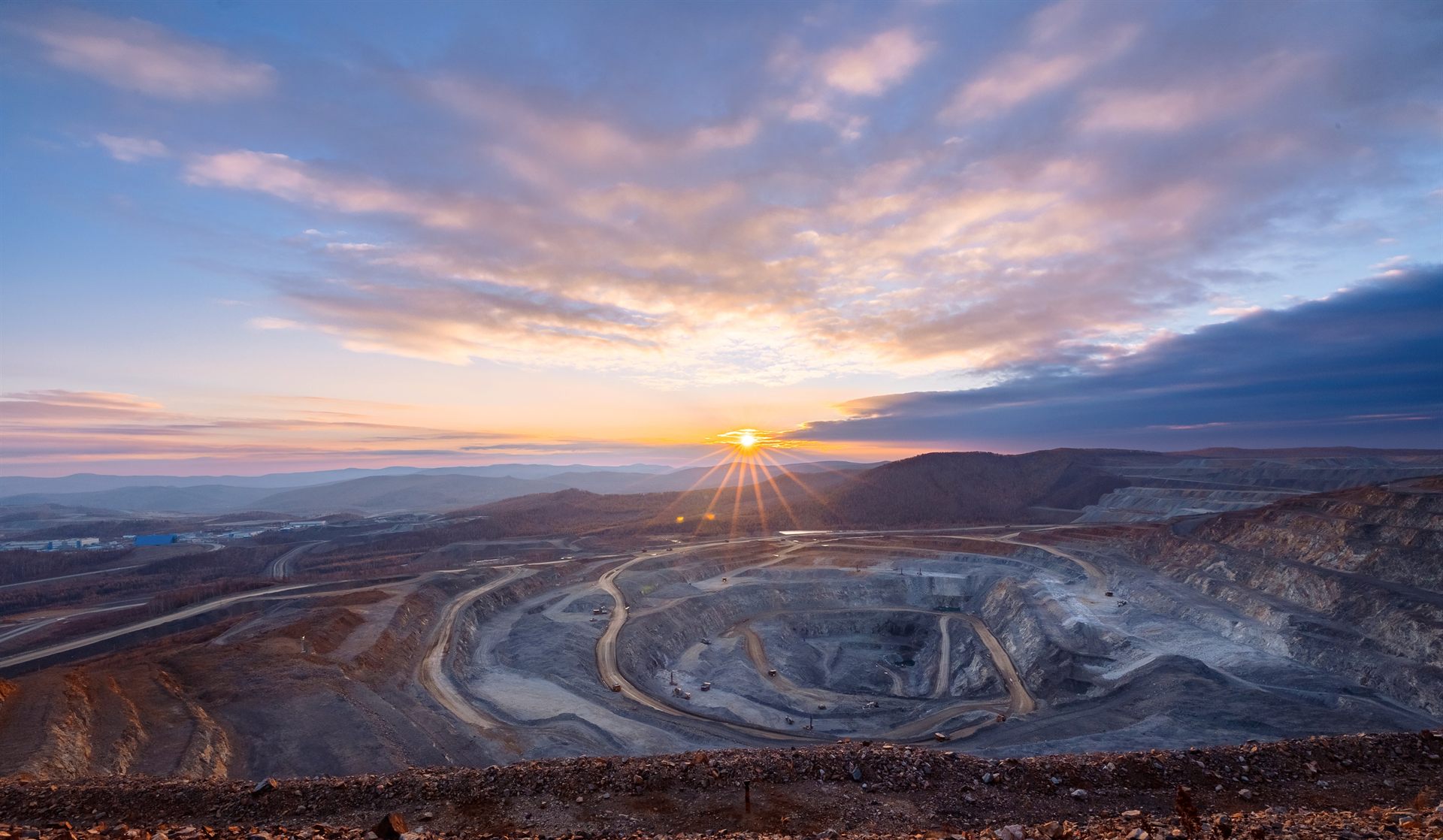 Open-pit mine at sunset with the sun setting over distant mountains