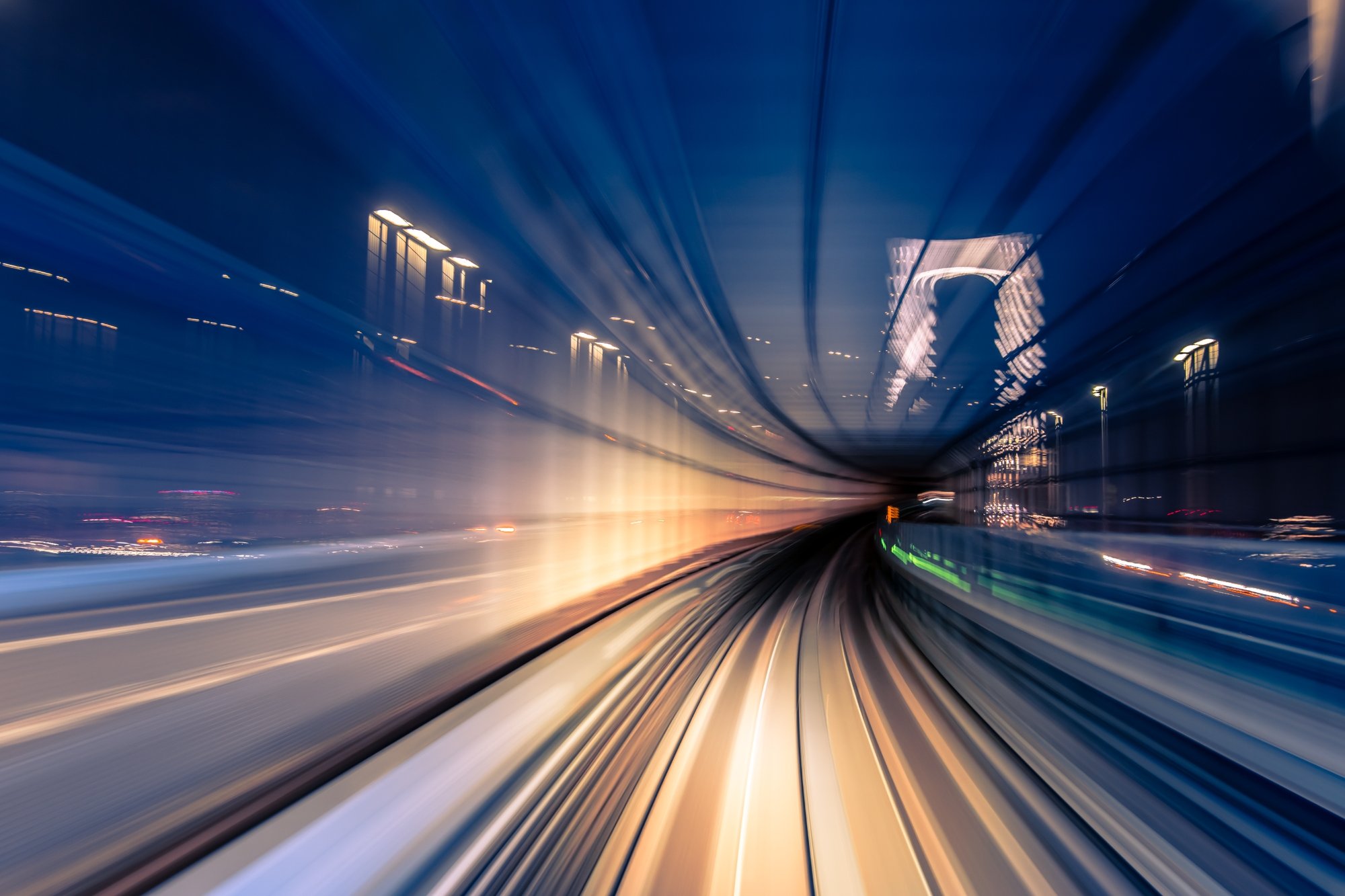 Motion-blurred view from a train moving through a city rail tunnel at night